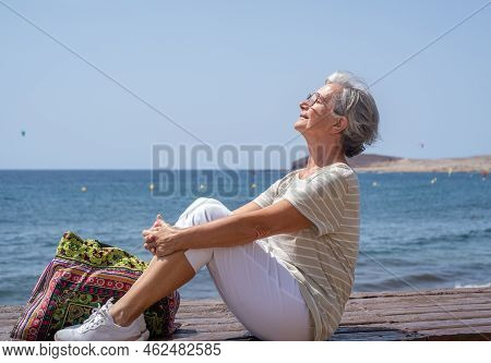 Happy Senior Woman Sitting Near The Beach With Her Face Facing The Sun - Elderly Beautiful Lady Rela