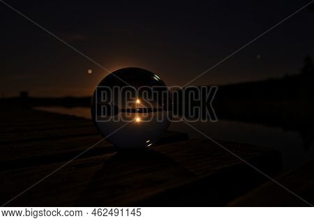 Glass Ball On A Wooden Pier At A Swedish Lake At Night. Stars And Moon In The Background. Nature Sho