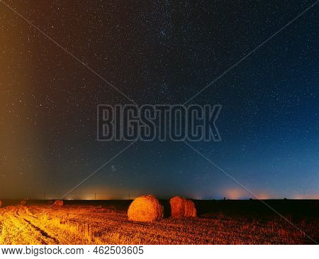 Night Starry Sky Above Rural Landscape Field Meadow With Rolls Of Straw In Fields After Harvest. Agr