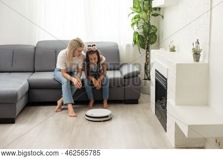Cute Child Near Mother Looking At Robotic Vacuum Cleaner In Living Room