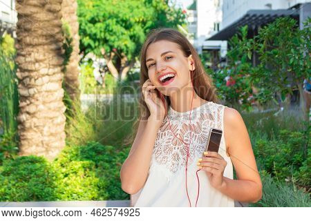 Beautiful Brownhair Woman Is Listening Music In Headphones In The Park. She Is Wearing Fashionable W