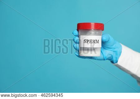 Scientist Holding Container With Sperm On Turquoise Background, Closeup. Space For Text