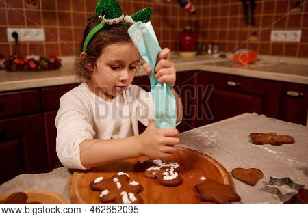 Beautiful Child, A Lovely Caucasian Little Girl In White Sweater And Elf Hoop, Squeezing Icing From 