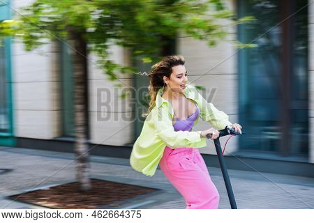 Happy Young Stylish Woman Riding Scooter And Smiling. Photo Is Blurred To Emphasize Speed