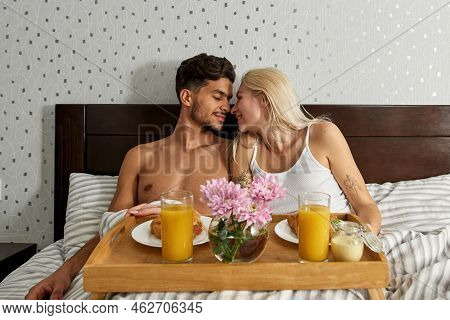 Young Joyful Mutiethnic Couple Touch Noses During Have Breakfast On Bed At Home. Middle Eastern Man 