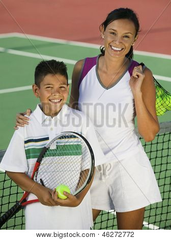 Ritratto di felice madre e figlio con palle e racchetta da rete sul campo da tennis
