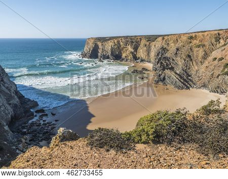 View Of Empty Praia Do Tonel Beach With Ocean Waves, Cliffs And Stones, Wet Golden Sand And Green Ve