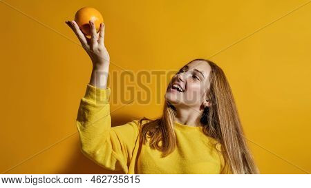 Cropped Image Of European Female Teenage Holding And Looking At Whole Orange In Hand. Girl Of Zoomer