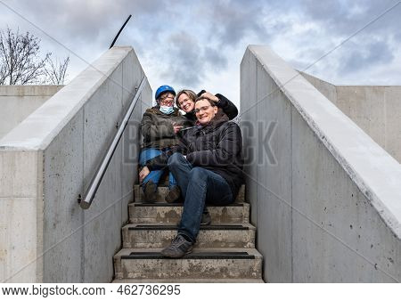 Family Portrait Of A Girl With Down Syndrome On Concrete Stairs With Her Adult Brother And His Attra