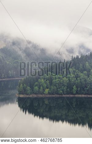 Rainy And Foggy Morning At The Sance Dam. Reflection Of Deciduous Forest On The Water Surface. Autum
