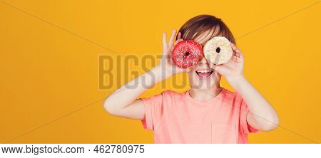 Happy Child Played With Donuts On Yellow Background Wall. Kid Enjoying Sweets. Cute Funny Boy Holdin