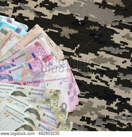Ukrainian Hryvnya Bills On Fabric With Texture Of Ukrainian Military Pixeled Camouflage. Cloth With 
