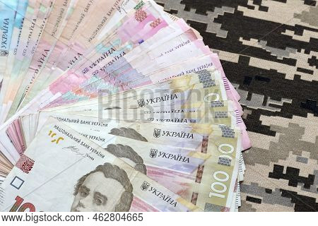Ukrainian Hryvnya Bills On Fabric With Texture Of Ukrainian Military Pixeled Camouflage. Cloth With 
