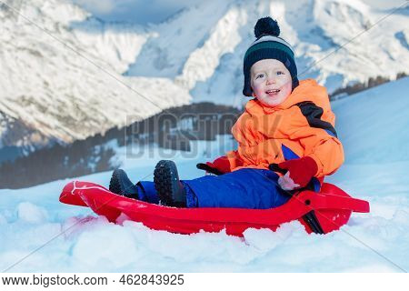 Little Boy Sit On Sledge In Show Over Mountains Going Downhill