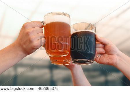 Male Hands Holding Three Glass Mugs Of Light And Dark Draft Beer. Beer Toast, Cheers