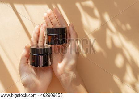 Two Jars Of Moisturizer In Women's Hands. Amber Glass Bottles With Gel, Shampoo, Cosmetic, Close-up 