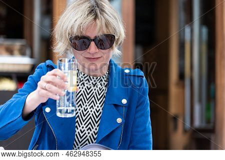 Attractive Thirty Year Old Woman With Sunglasses Drinking A Glass Of Water On A Terrace, Belgium