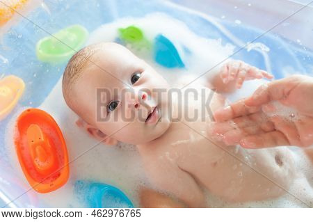 Baby Bath Time. Close-up Detail View Of Mother Bathing Cute Little Peaceful Baby In Tub With Water A