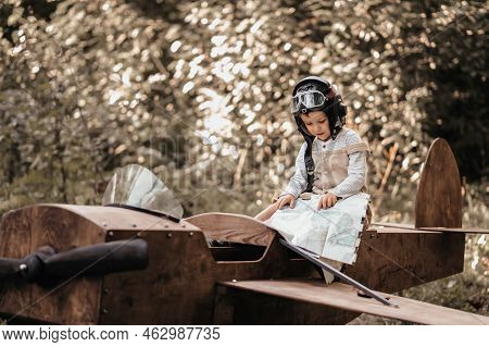 A Young Boy Aviator On A Homemade Airplane In A Natural Landscape With A Geographical Map In His Han