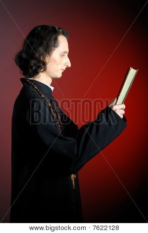 Fogalmi portré imádkozott a pap egy fából készült kereszt olvasás Szent Biblia. Piros háttér