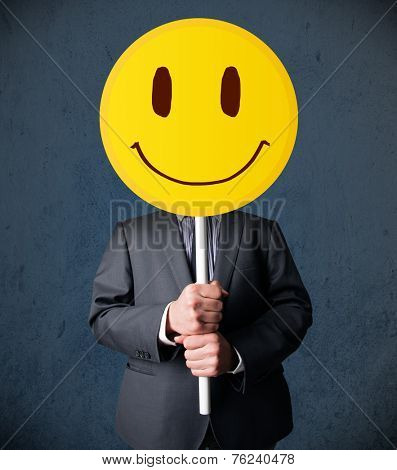 Businessman holding a yellow smiley face emoticon in front of his head