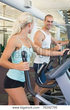 Side view of a fit young couple working on x-trainers at the gym