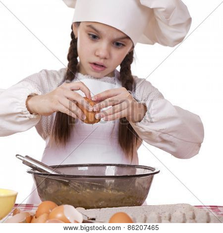 Little girl in a white apron breaks eggs in a deep dish, sharpness on hand and egg
