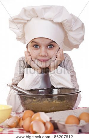 Little girl in a white apron breaks near the plate with eggs, isolated on white background