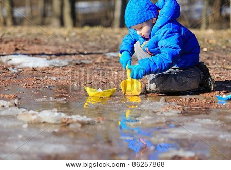 little boy plaing with paper boats in spring puddle