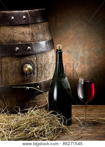 Still-life with glass of wine, bottle and barrel on the table in the cellar.