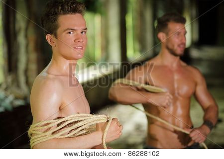 two young men stripped to waist is wrapped rope in his hands in abandoned building focus on left man 