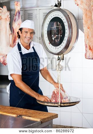 Portrait of confident male butcher weighing meat on scale in butchery