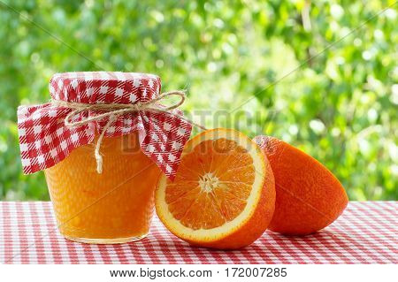 Jar of orange jam and orange halves on a red checkered tablecloth
