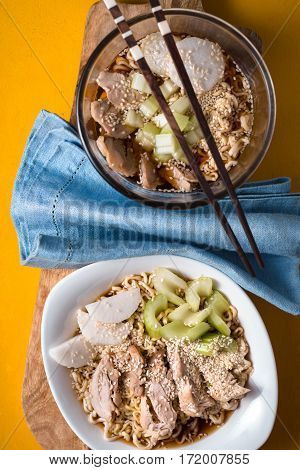 Two bowls of soup noodle ramen celery chicken and blue napkin vertical