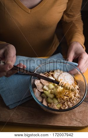 Woman eating soup with ramen noodles with chicken and celery vertical