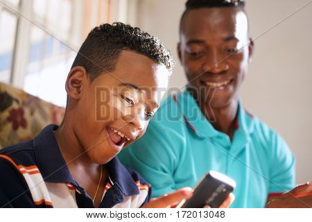 Happy black family at home. African american father and child playing game with cell phone. Hispanic dad and son having fun with smartphone.