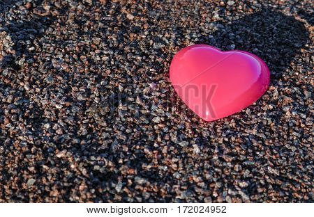 Red plastic heart lies on the sand. pea gravel.