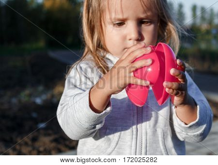 Little Girl Playing With A Red Plastic Heart. She Holds It In Her Hands