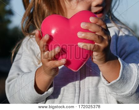 Little Girl Playing With A Red Plastic Heart. She Holds It In Her Hands