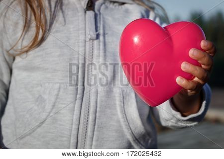 Little Girl Playing With A Red Plastic Heart. She Holds It In Her Hands