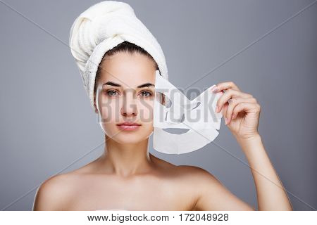 Girl with almost rended white mask. Model pulling away mask from her face. Hair wrapped with towel. Head and shoulders, studio, indoors
