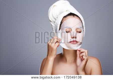 Girl rending white mask. Model pulling away mask from her face. Closed eyes. Head and shoulders, studio, indoors