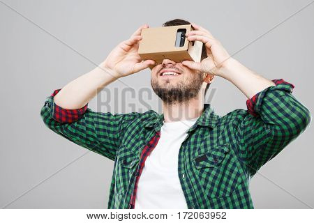 Man in green checked T-shirt looking at vr box, Virtual Reality Glasses, cardbox. Waist up. Indoors, studio