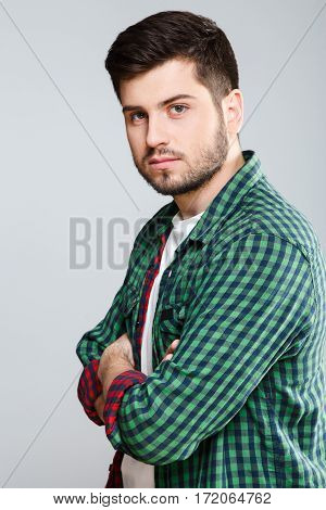 Man in green checked T-shirt turned aside, looking at camera. Young man, casual style. Half turn, waist up. Hands crossed. Indoors, studio