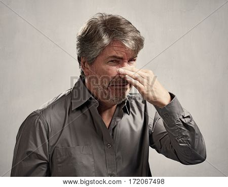 Man hiding his nose bad smell over gray background.
