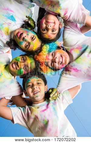 five Indian kids making circle on holi, Asian small kids or siblings or friends with heads together in round, with faces coloured with gulal