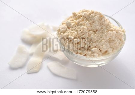 Coconut flour and flakes on white background. Cream powder in a glass bowl. Isolated on white. Alternative gluten-free flour for baking and cooking