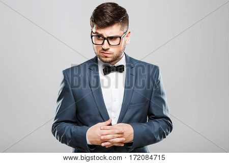 Stylish young man in suit with bow and eyeglasses. Fingers crossed, looking aside with contempt. Jacket, bow, official outlook. Waist up, studio, indoors