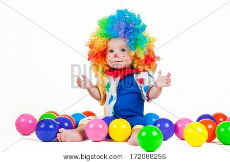 Child clown with a red nose and multicolored wig in with toy balls on a white background.