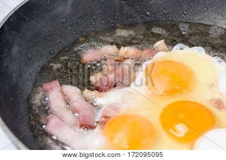 Frying eggs with sliced bacon in the hot oil.